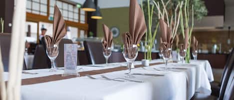 A restaurant with white tablecloths, neatly folded brown napkins, and clear glassware.