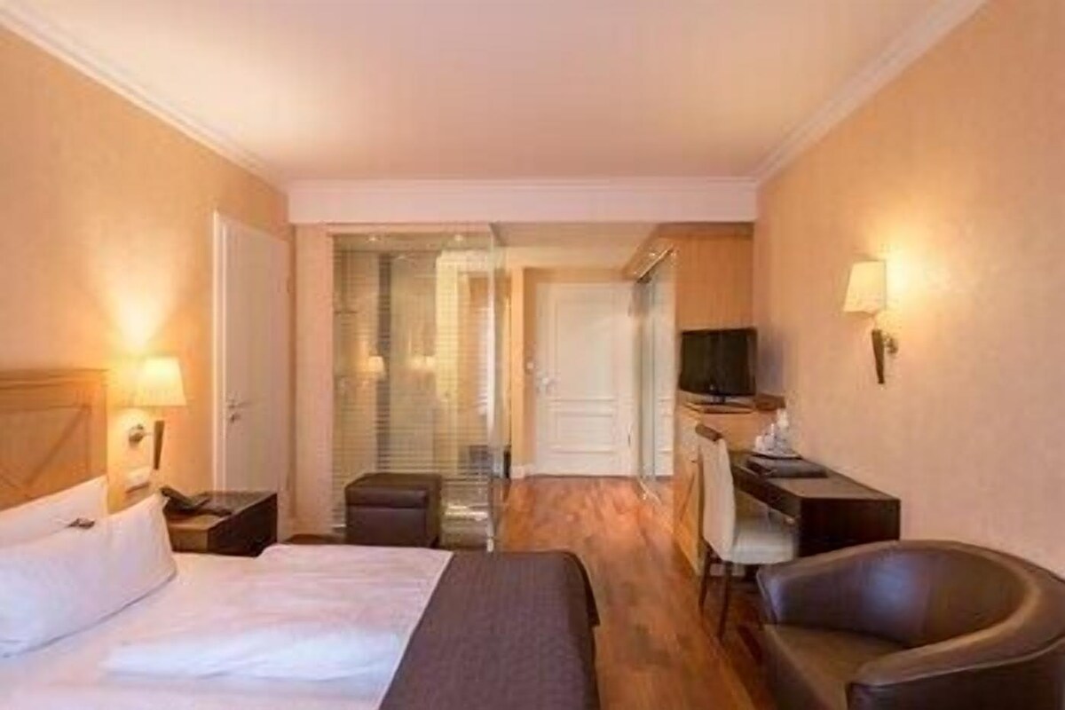 Een hotelkamer met een bed, een bureau, een stoel, een televisie en een kleine kitchenette.