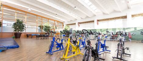 Une salle de sport spacieuse équipée de nombreux vélos d’exercice et d’appareils de cardio, dotée d’un plancher en bois et de grandes fenêtres laissant entrer la lumière naturelle.