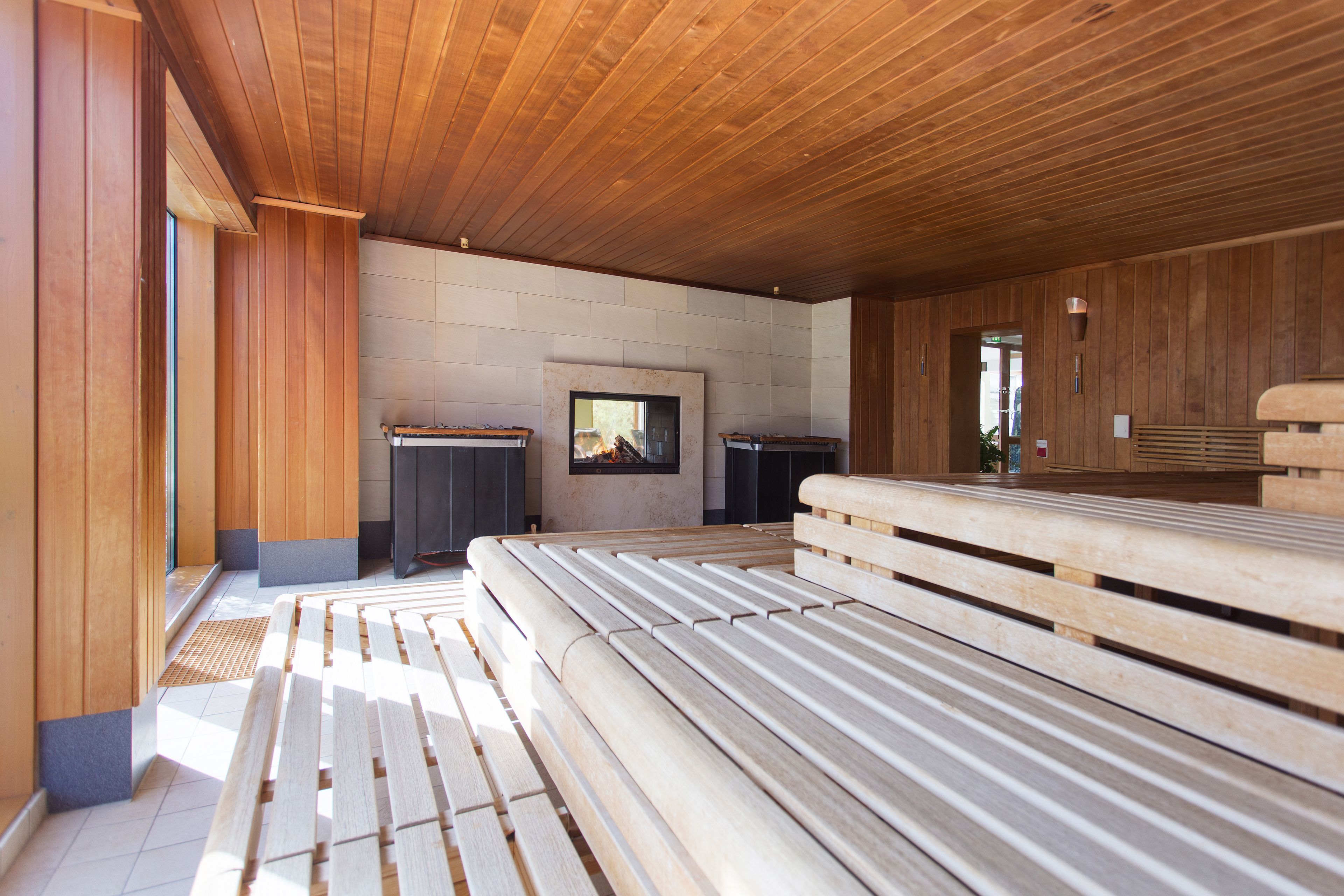 A modern interior with wooden benches, a fireplace, and a stone wall.