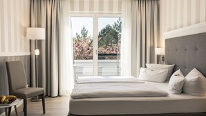 Une chambre d’hôtel avec un grand lit, une chaise, une table avec des fruits et une vue sur les arbres par la fenêtre.