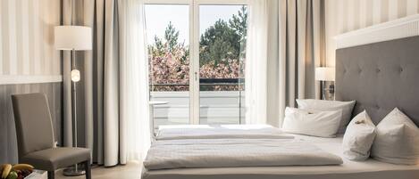 A hotel room with a large bed, a chair, a table with fruit, and a view of trees through the window.