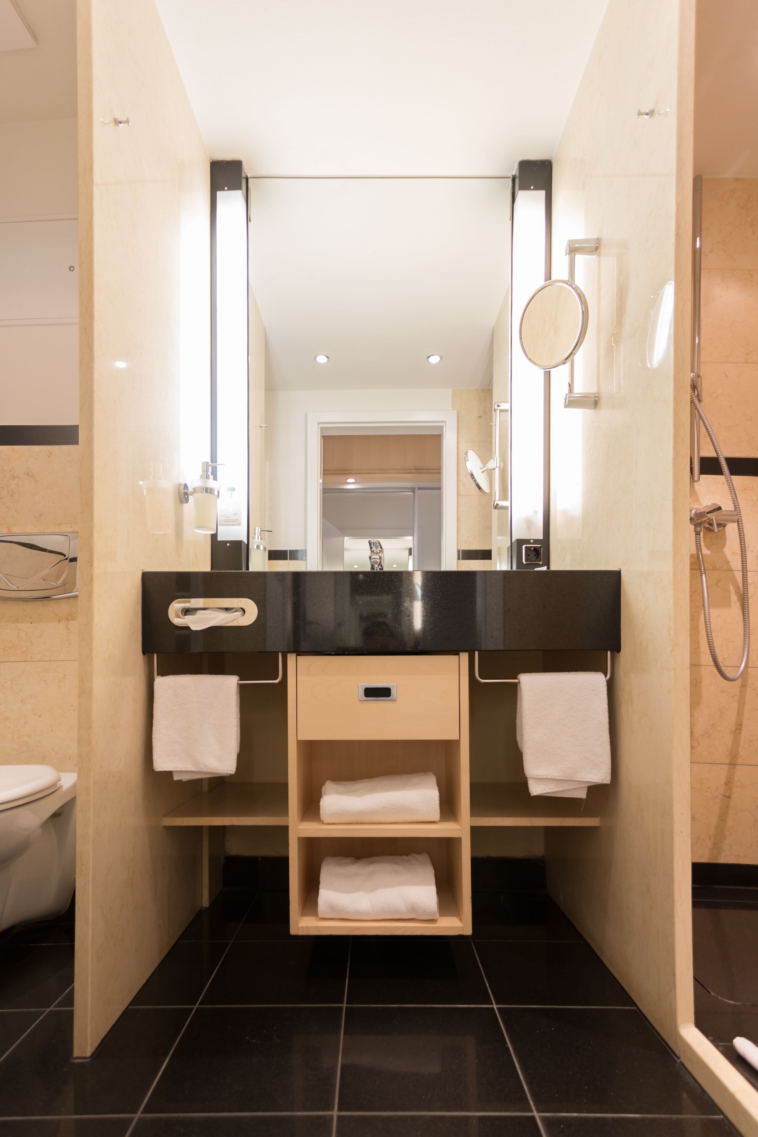 A modern bathroom with a black countertop, a mirror, a towel rack, and a shower.