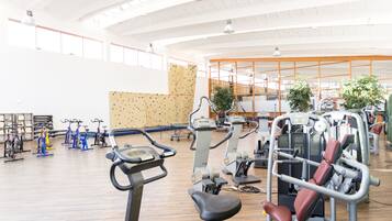 A spacious gym with various exercise machines, a climbing wall, and large windows allowing natural light.
