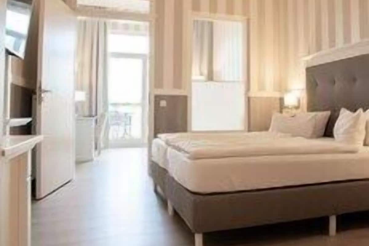 Ein Hotelzimmer mit Bett, Nachttischen, einem Kleiderschrank, einem Fenster und einer Tür, die auf einen Balkon führt.