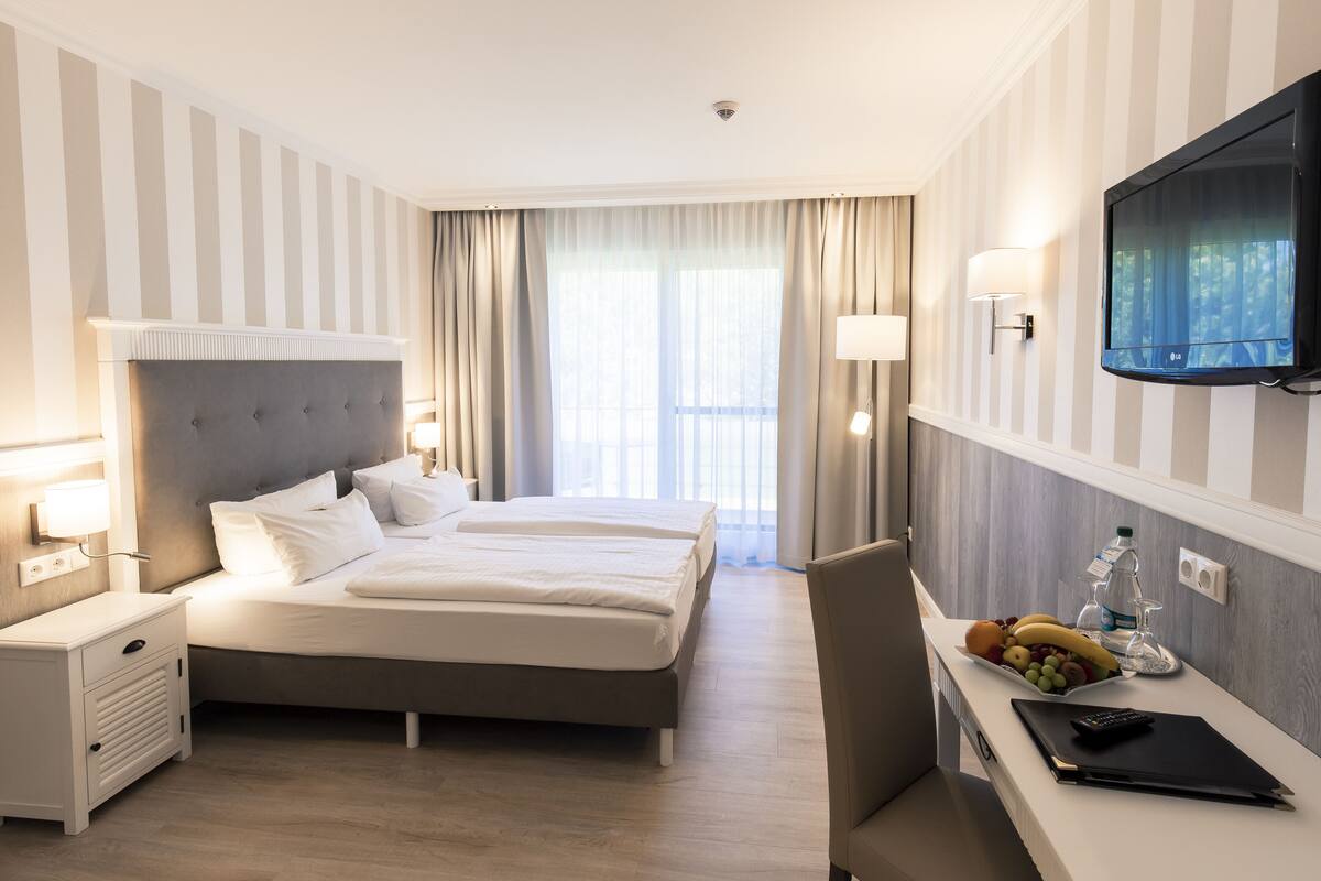 Ein Hotelzimmer mit Bett, Nachttischen, Schreibtisch mit Stuhl, Fernseher und einem fensterbepflanzten Fenster.