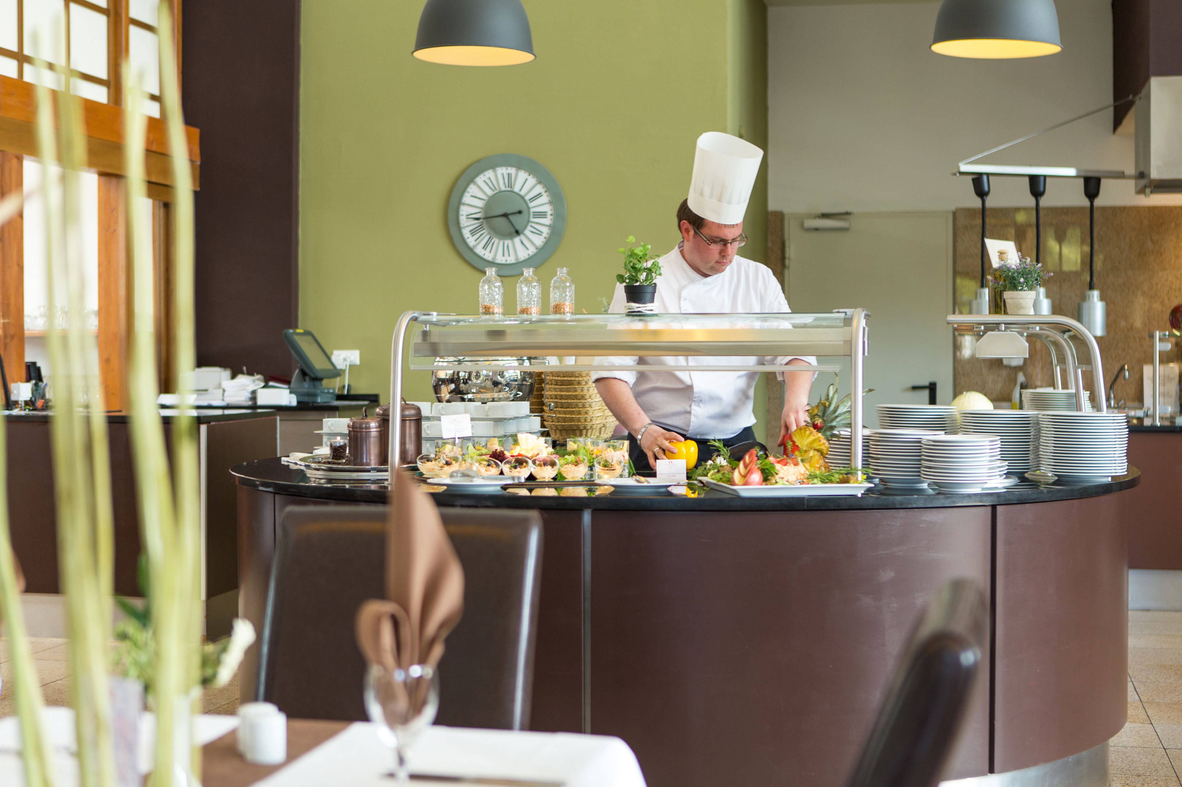 Un buffet où un chef prépare les plats, une horloge au mur et un décor intérieur moderne.