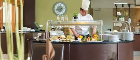 Un buffet où un chef prépare les plats, une horloge au mur et un décor intérieur moderne.
