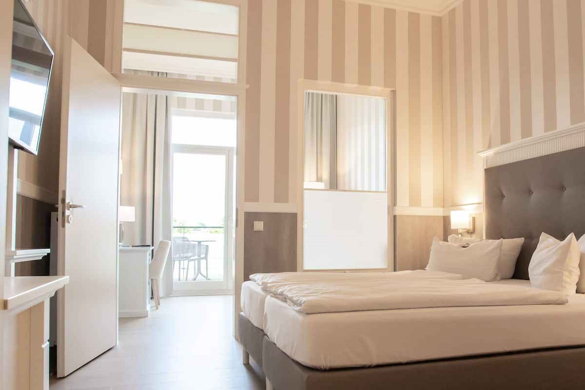 Ein Hotelzimmer mit einem großen Bett, einem Fernseher, einem Schreibtisch und einem Balkon mit Blick.