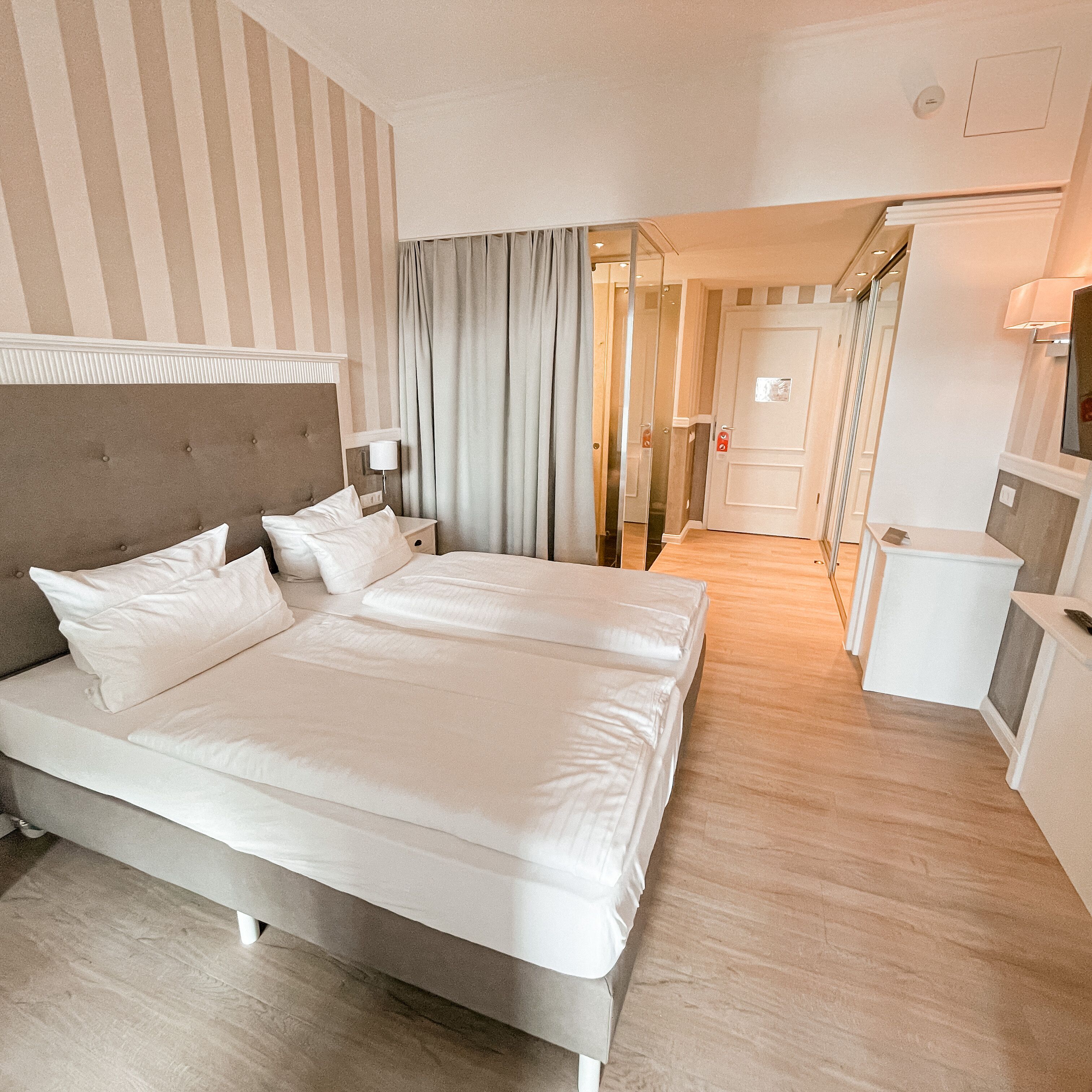 A hotel room with a large bed, a bedside table, a lamp, and a mirror.