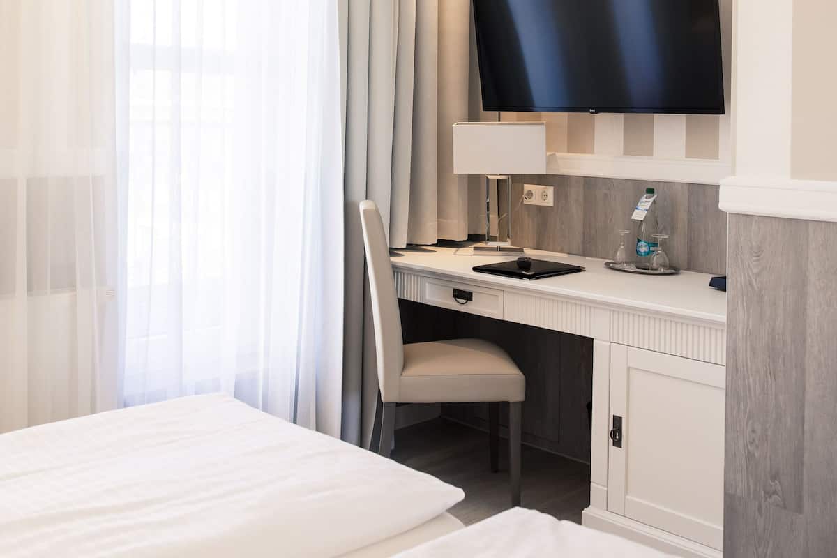 Ein Hotelzimmer mit einem Bett, einem Schreibtisch mit Stuhl, einem Fernseher und einem Fenster mit Vorhängen.