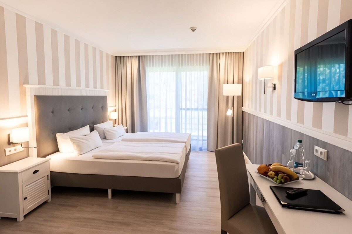 Une chambre d’hôtel comprenant un lit, des tables de chevet, un bureau avec une chaise, un téléviseur à écran plat et des rideaux.