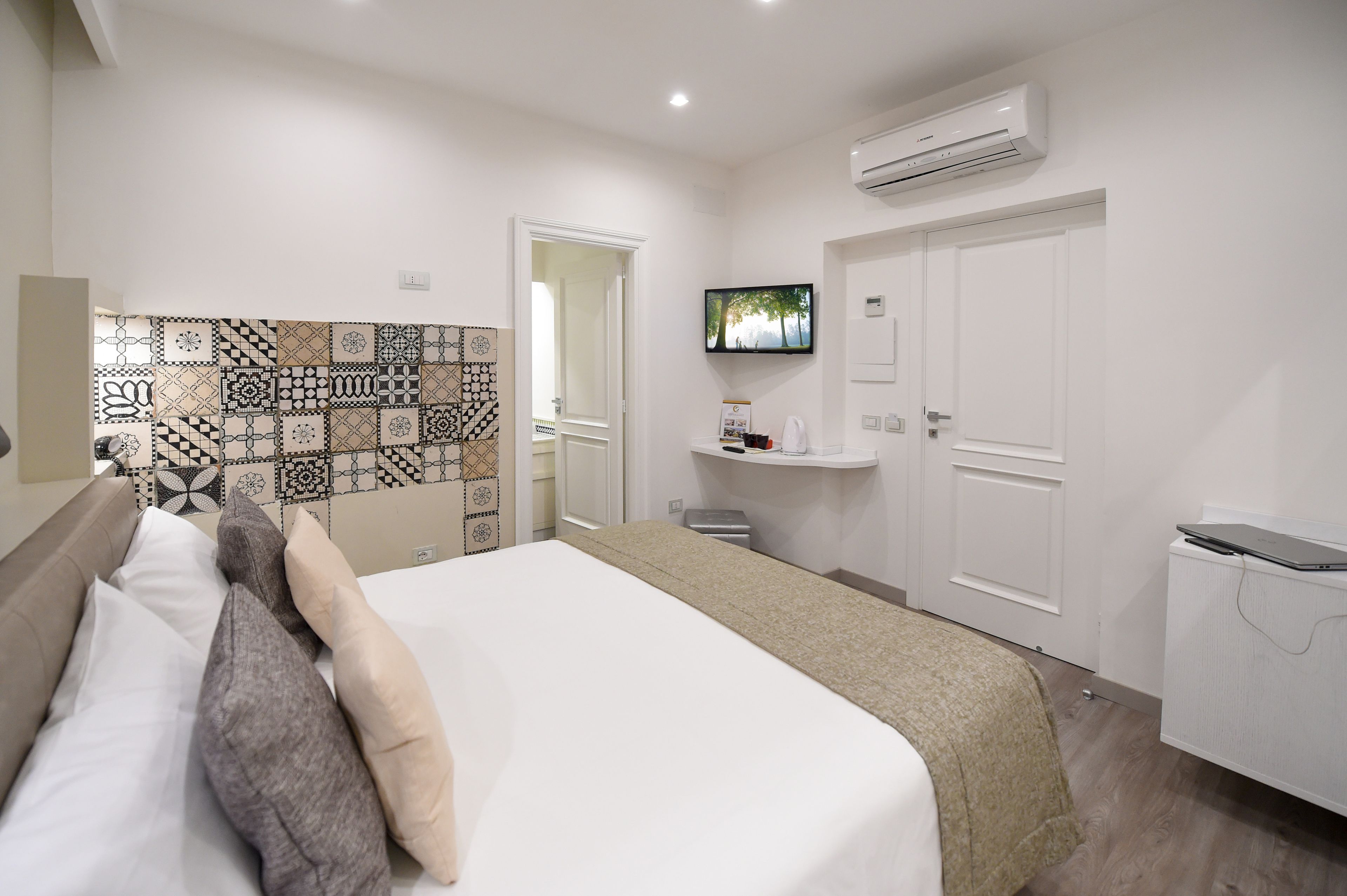 Una habitación de hotel con cama, televisión, escritorio y laptop, además de un equipo de aire acondicionado.