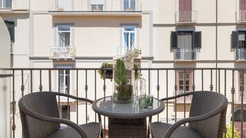Un balcon avec des fauteuils en osier, une table en verre et un vase rempli de fleurs.