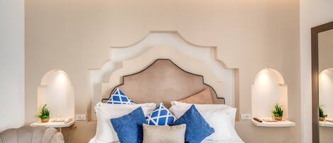 Un dormitorio ordenado con una cama grande, mesitas de noche, una silla y un espejo.