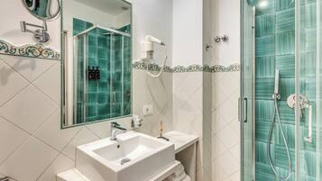 Un baño con un lavamanos blanco, un espejo, un secador de pelo portátil y una ducha con paredes de vidrio.