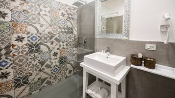 A bathroom with a tiled shower wall, a white sink, a mirror, and two baskets on the countertop.