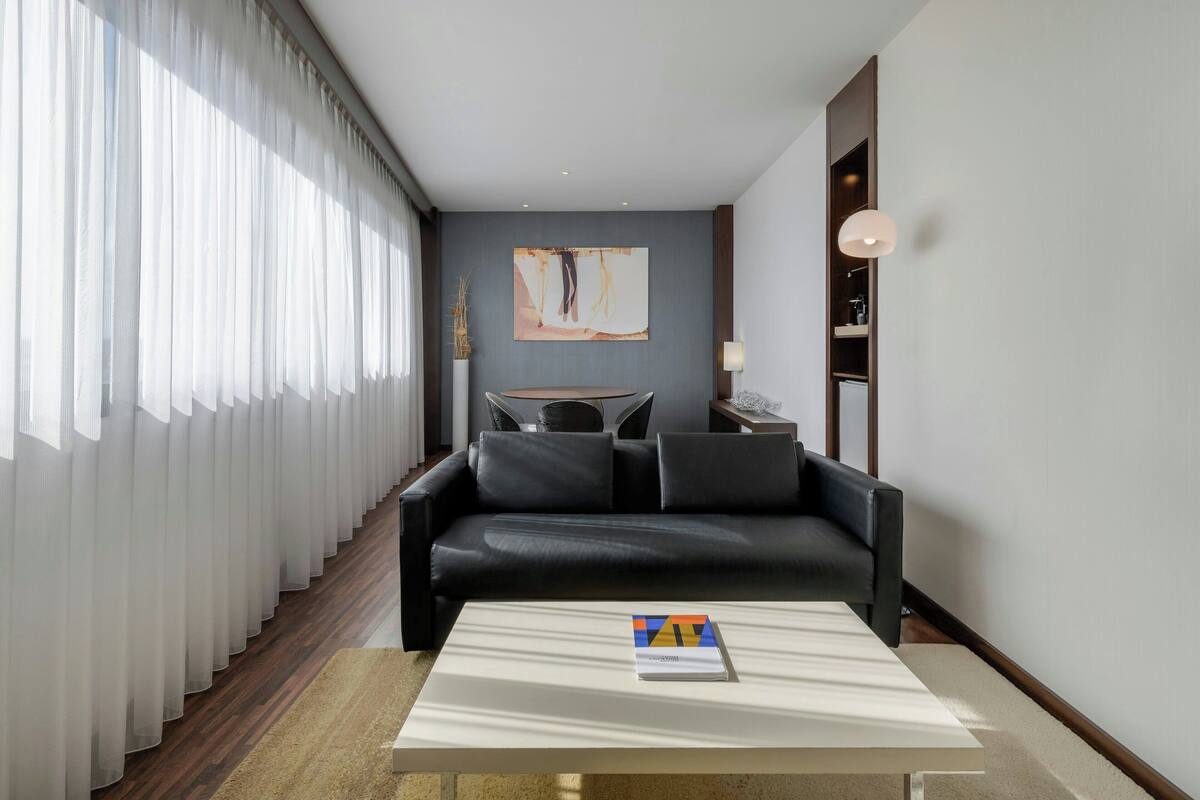 Una sala de estar moderna con un sofá de cuero negro, una mesa de centro blanca y un cuadro abstracto grande en la pared.