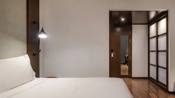 Un dormitorio con una cama, una mesita de noche, una lámpara de pared y una puerta corrediza que da a otra habitación.