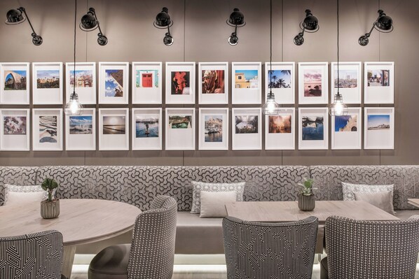 A modern dining area with a patterned bench, round tables, and framed pictures on the wall.