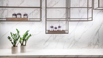 A marble countertop with two potted plants and three shelves with bottles.