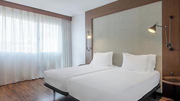 A hotel room with two beds, a large window with sheer curtains, a round table, and a textured wall panel.