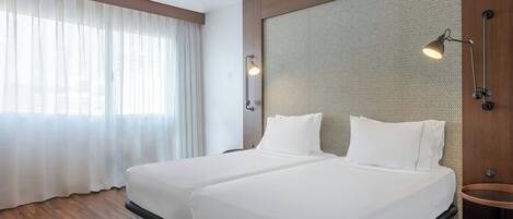 A hotel room with two beds, a large window with sheer curtains, a round table, and a textured wall panel.