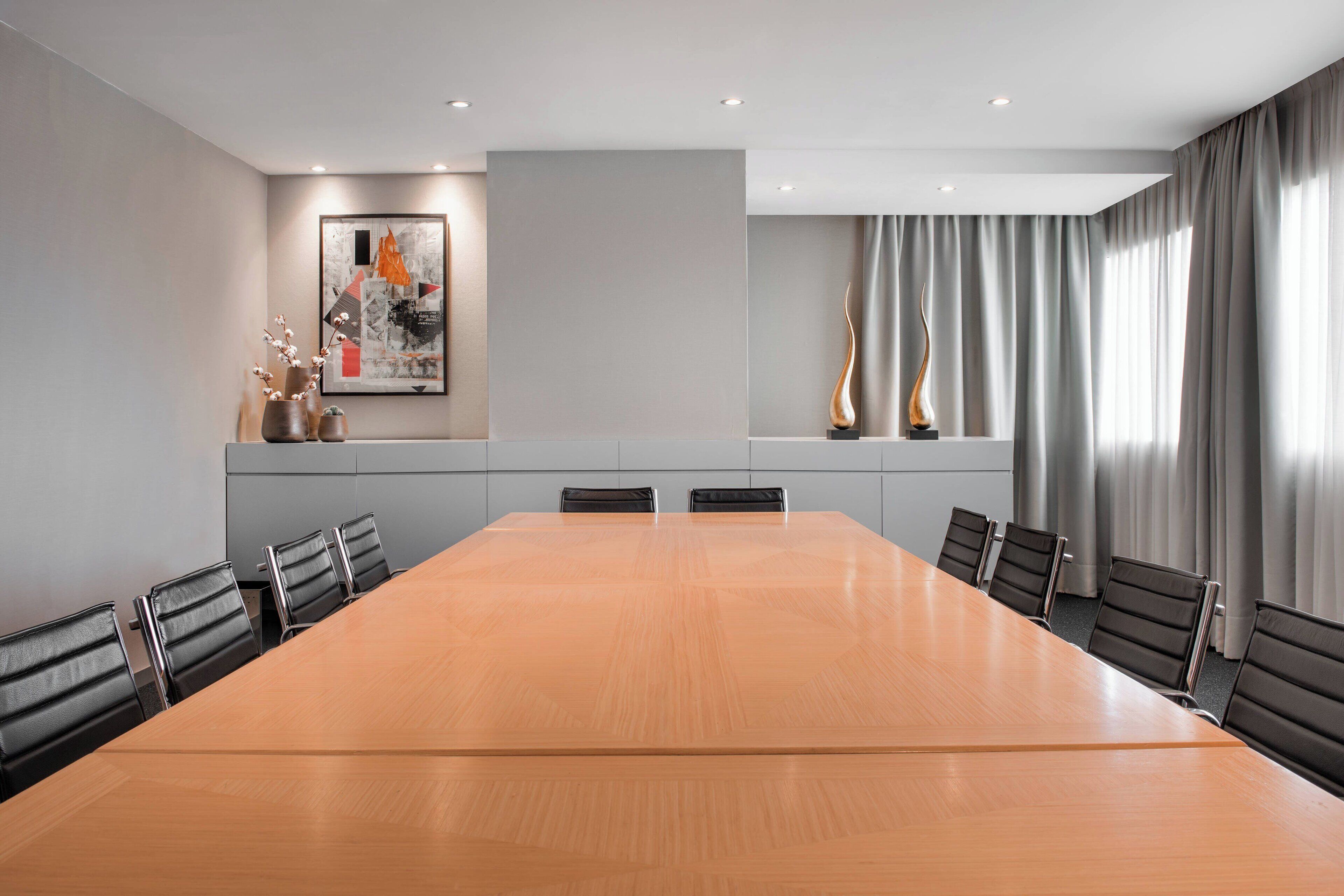 A conference room with a large wooden table, six chairs, a framed abstract painting, and a sculpture on the wall.