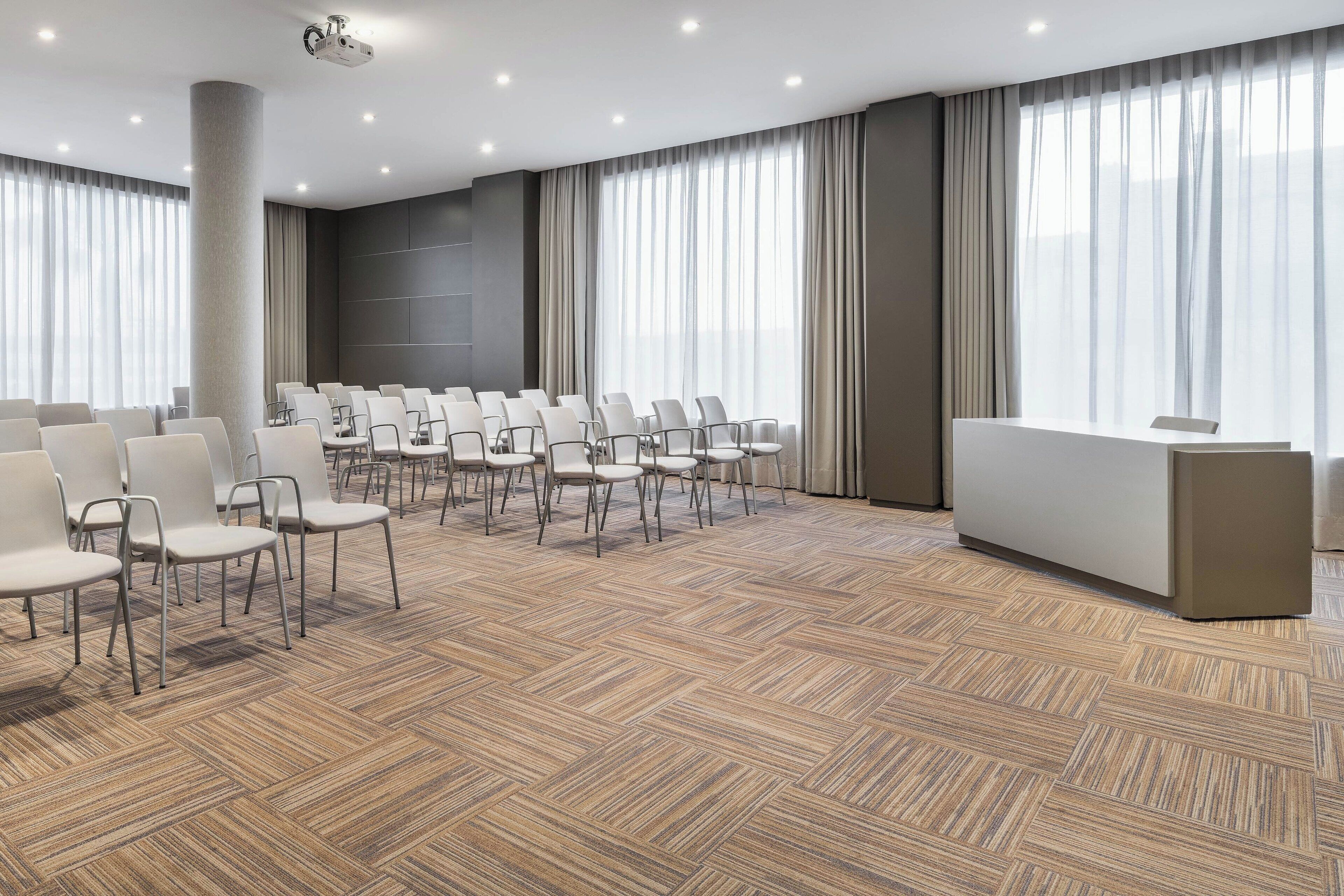 Une salle de conférence avec des rangées de chaises, un pupitre et une grande fenêtre avec des rideaux.