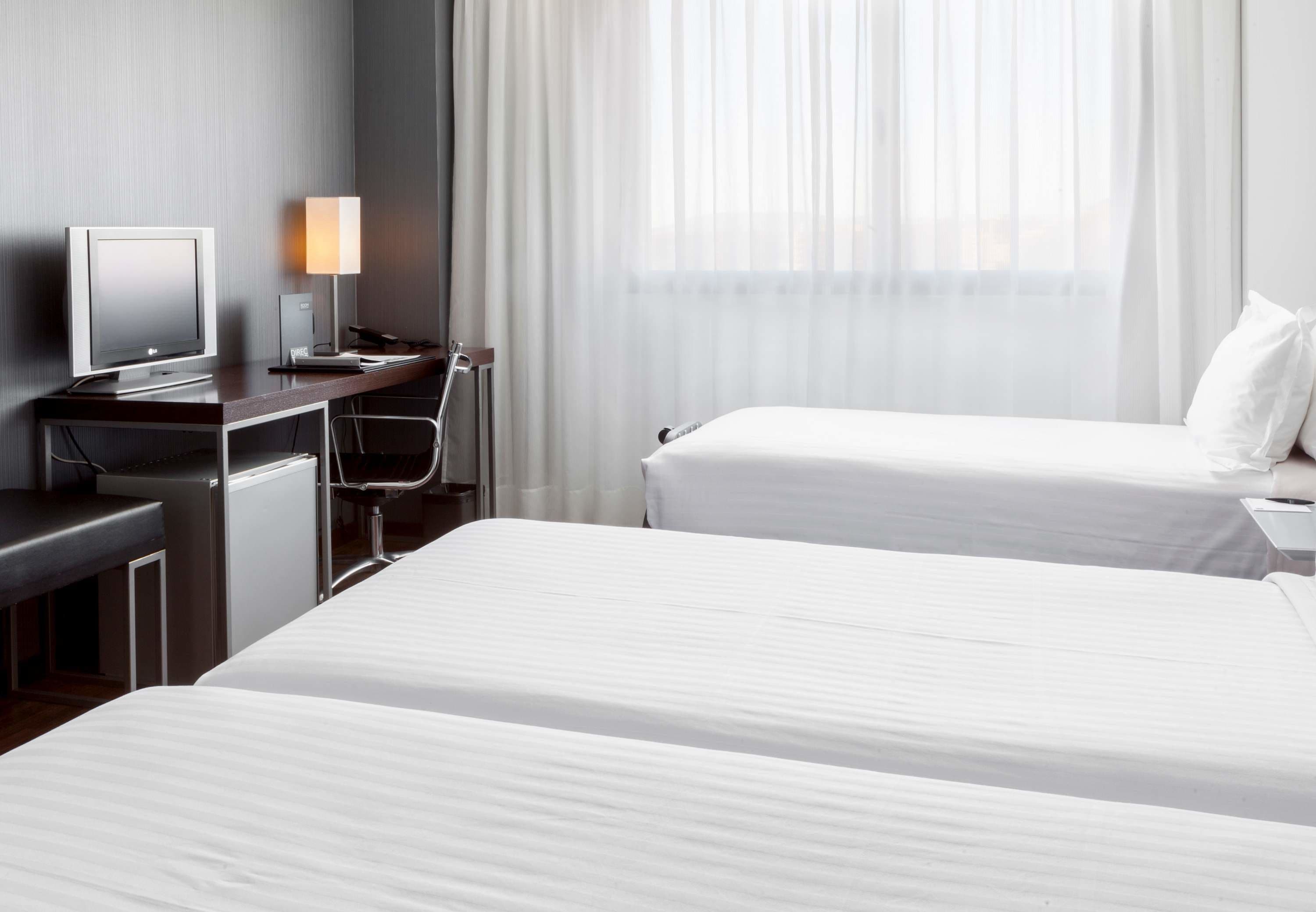 A hotel room with two beds, a desk with a computer, a lamp, and a chair.