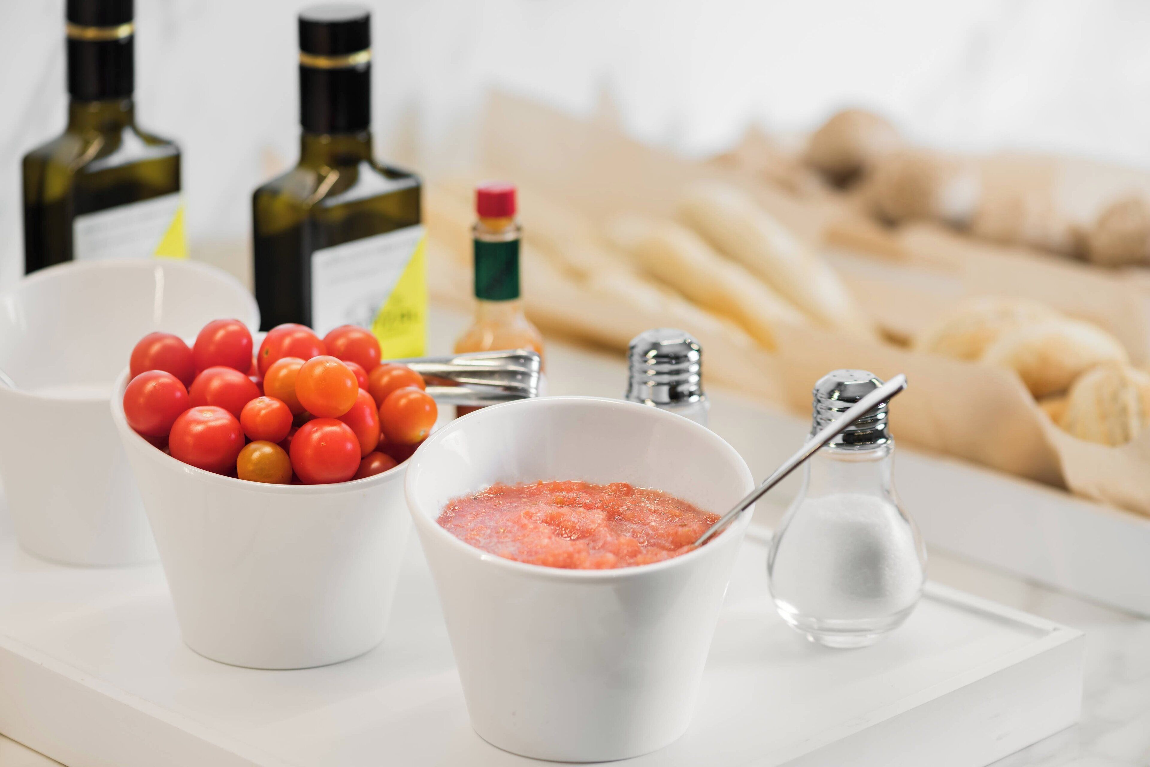 A tray with a bowl of cherry tomatoes, a bowl of pink sauce, and a salt shaker.
