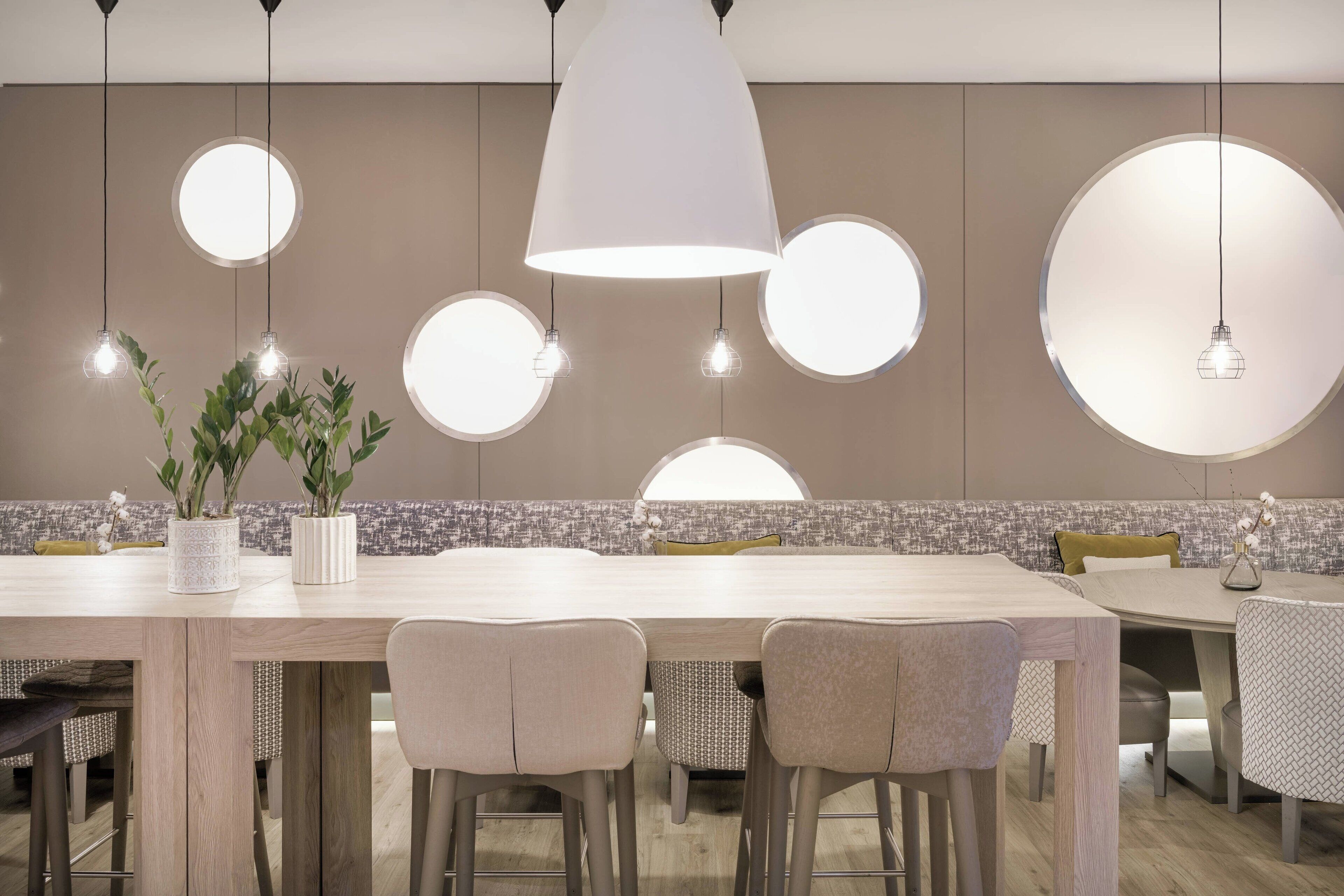 Een moderne eetruimte met een lange houten tafel, meerdere stoelen en hanglampen met ronde kappen.