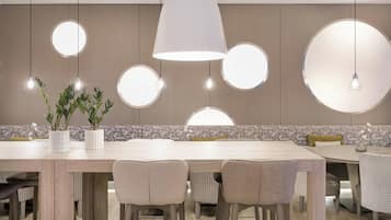 Una zona de menjador moderna amb una taula de fusta llarga, diverses cadires i il·luminació amb penjants i pantalla rodona.