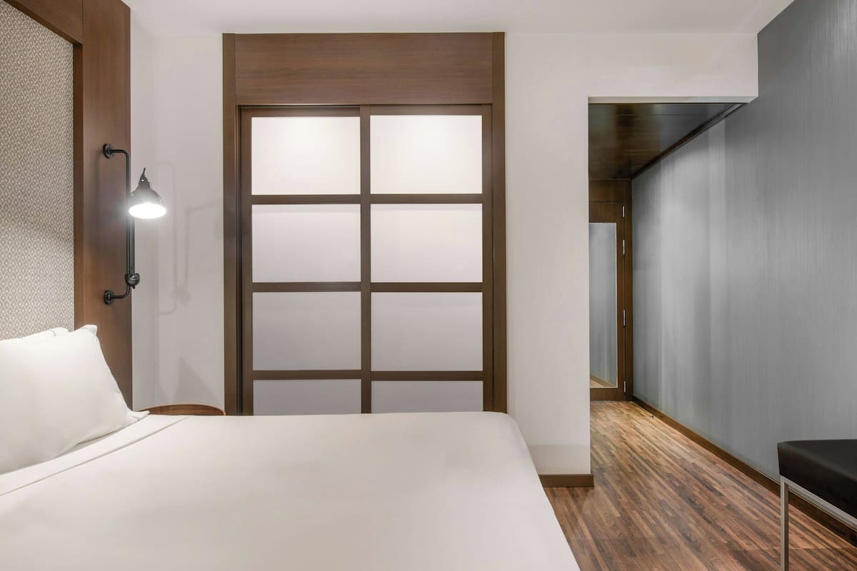Habitación de hotel con cama, mesita de noche, lámpara de pared y puerta corredera.