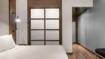 Habitación de hotel con cama, mesita de noche, lámpara de pared y puerta corredera.