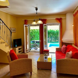 A living room with wicker furniture, a flat-screen TV, and a view of a swimming pool.