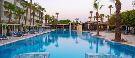A swimming pool with blue tiles, surrounded by lounge chairs and palm trees.