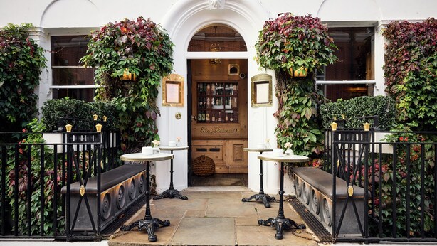 A traditional pub entrance with a wooden door, two round tables with benches, and a black wrought iron fence. - Durrants Hotel (London)