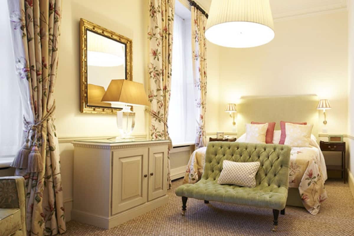 Une chambre d’hôtel avec un lit, un fauteuil vert, une commode et un miroir.