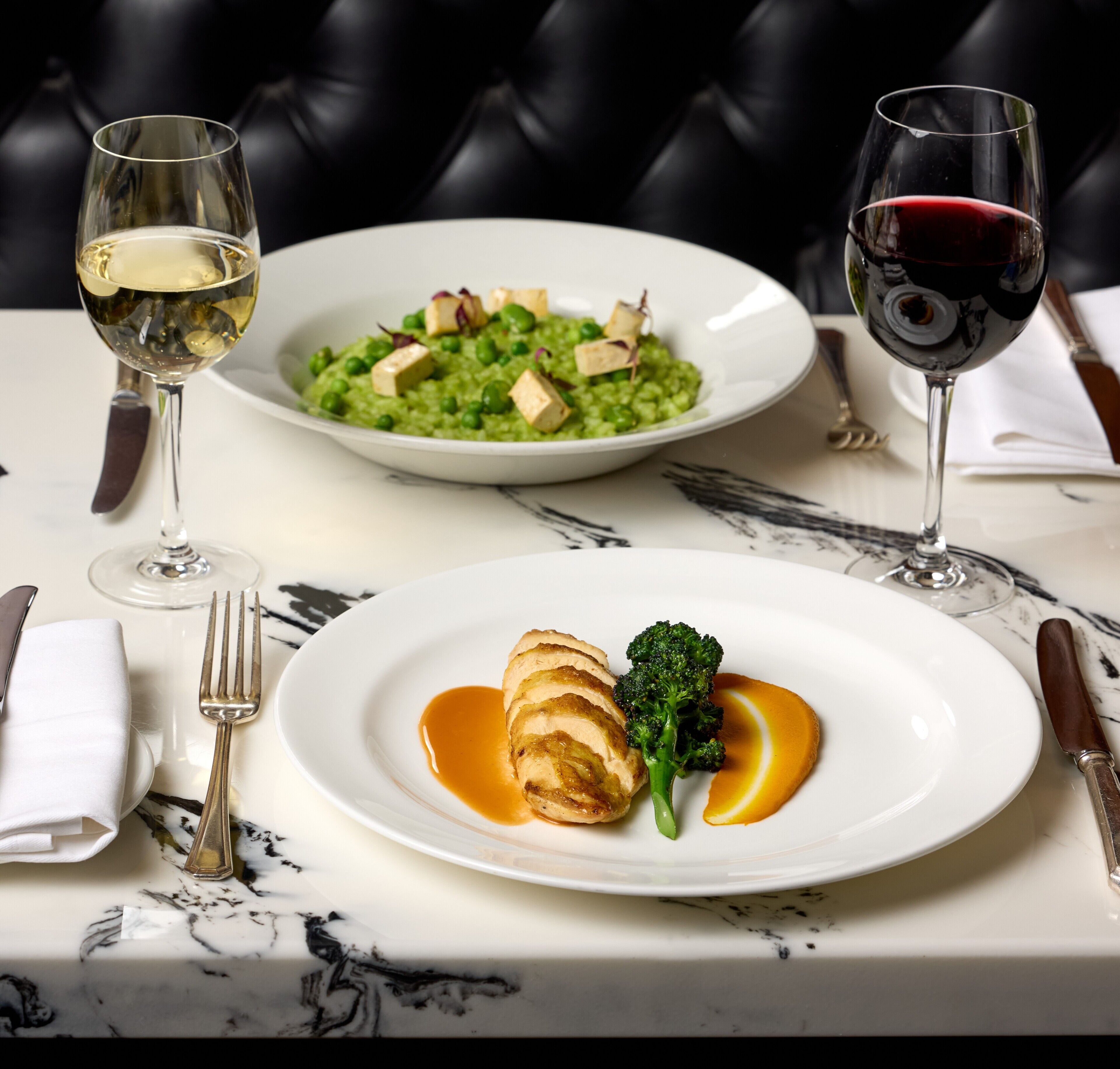 A dining table with plates of food, wine glasses, and cutlery.