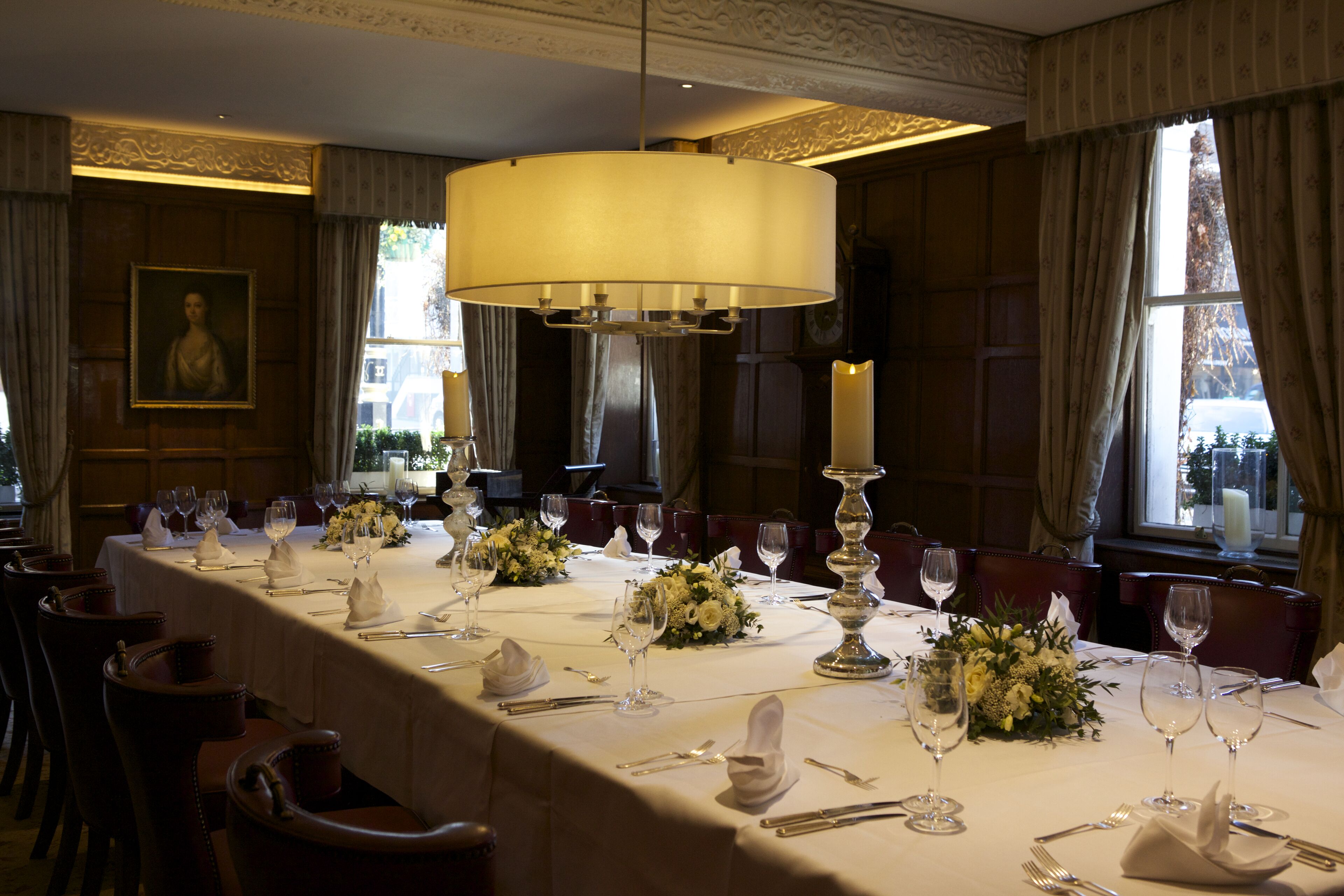 A formal dining room with a long table set for a meal, elegant chairs, and a chandelier.