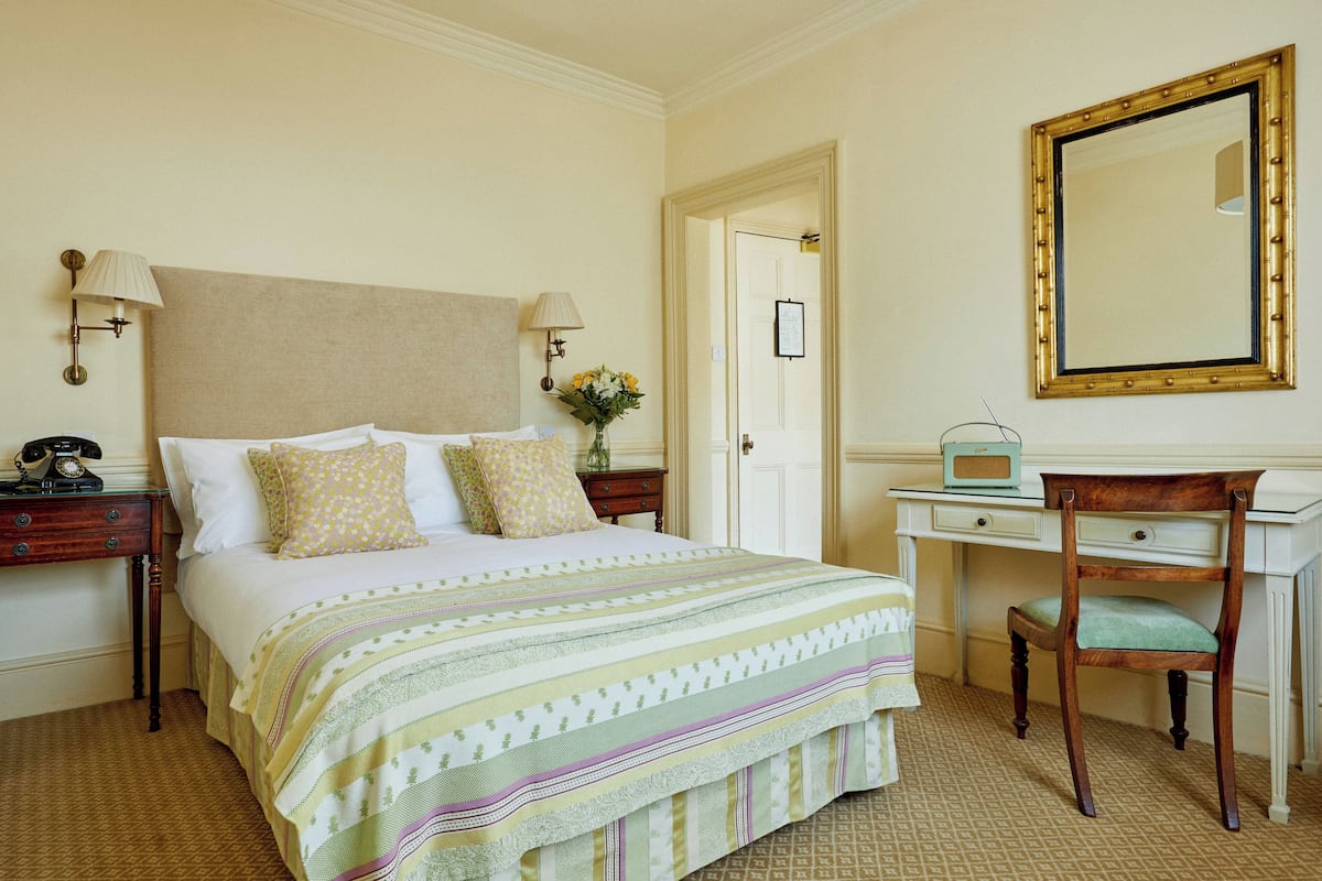 Une chambre d’hôtel comprenant un lit, des tables de chevet, un bureau, une chaise et un grand miroir.