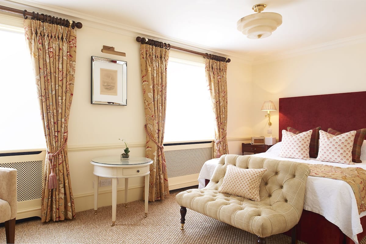 Une chambre avec un grand lit, une chaise, une petite table et des rideaux.