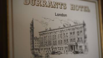 A framed illustration of the Durrants Hotel in London, featuring a classical building facade with detailed stonework and a vintage car in front.