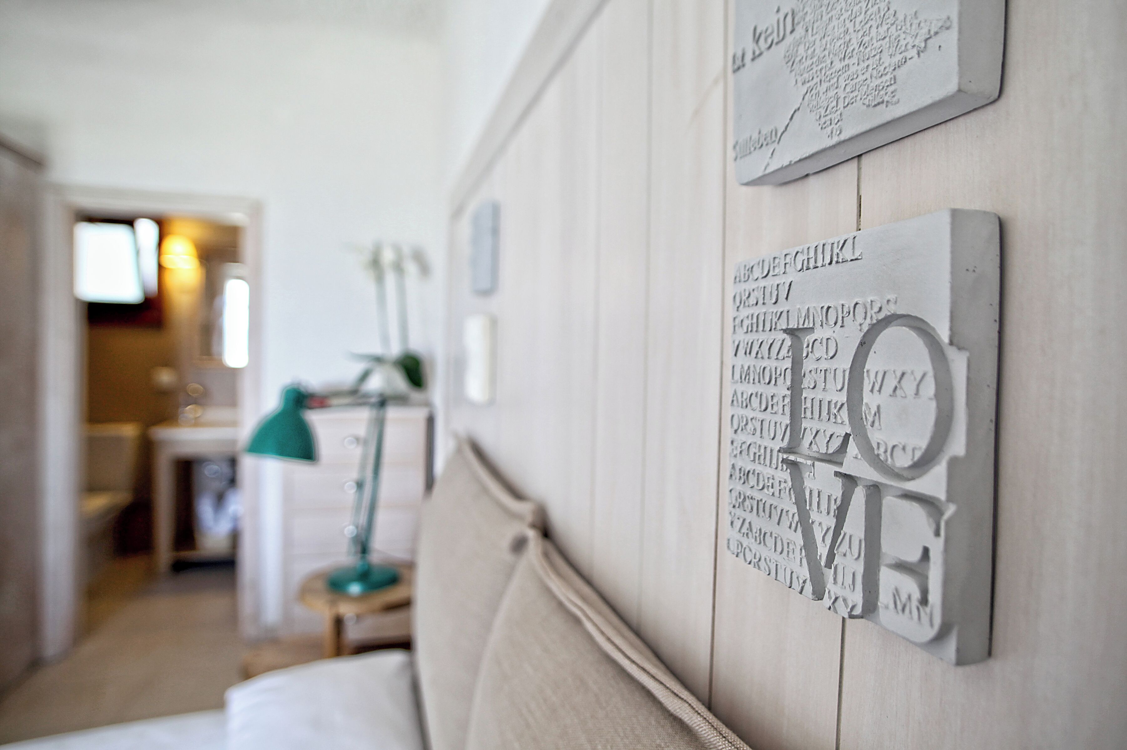 Une chambre avec un lit, une table de chevet, une lampe et un mur orné de lettres de l’alphabet et du mot « AMOUR ».