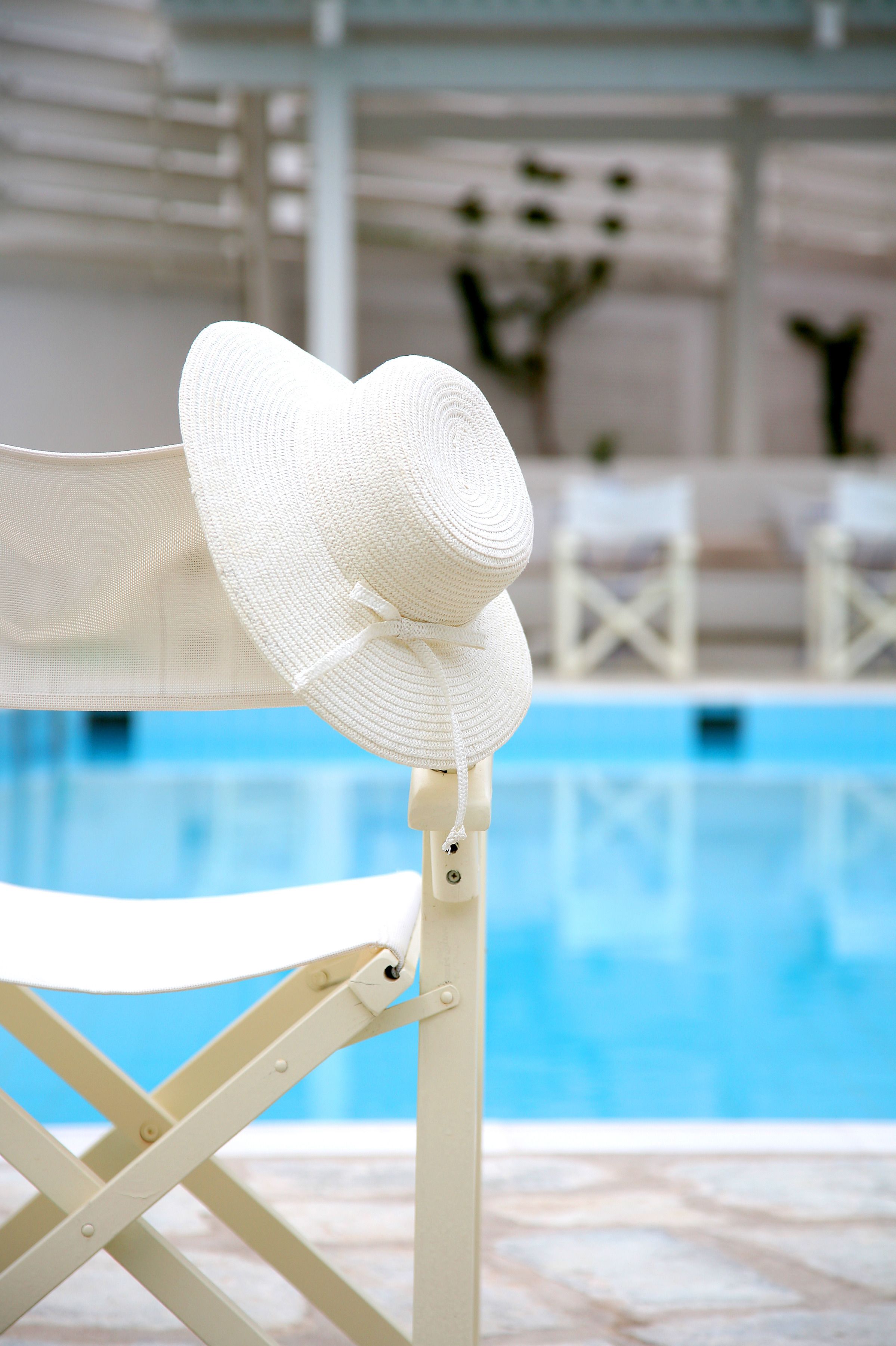 Una silla plegable blanca junto a una piscina, con un sombrero blanco encima.
