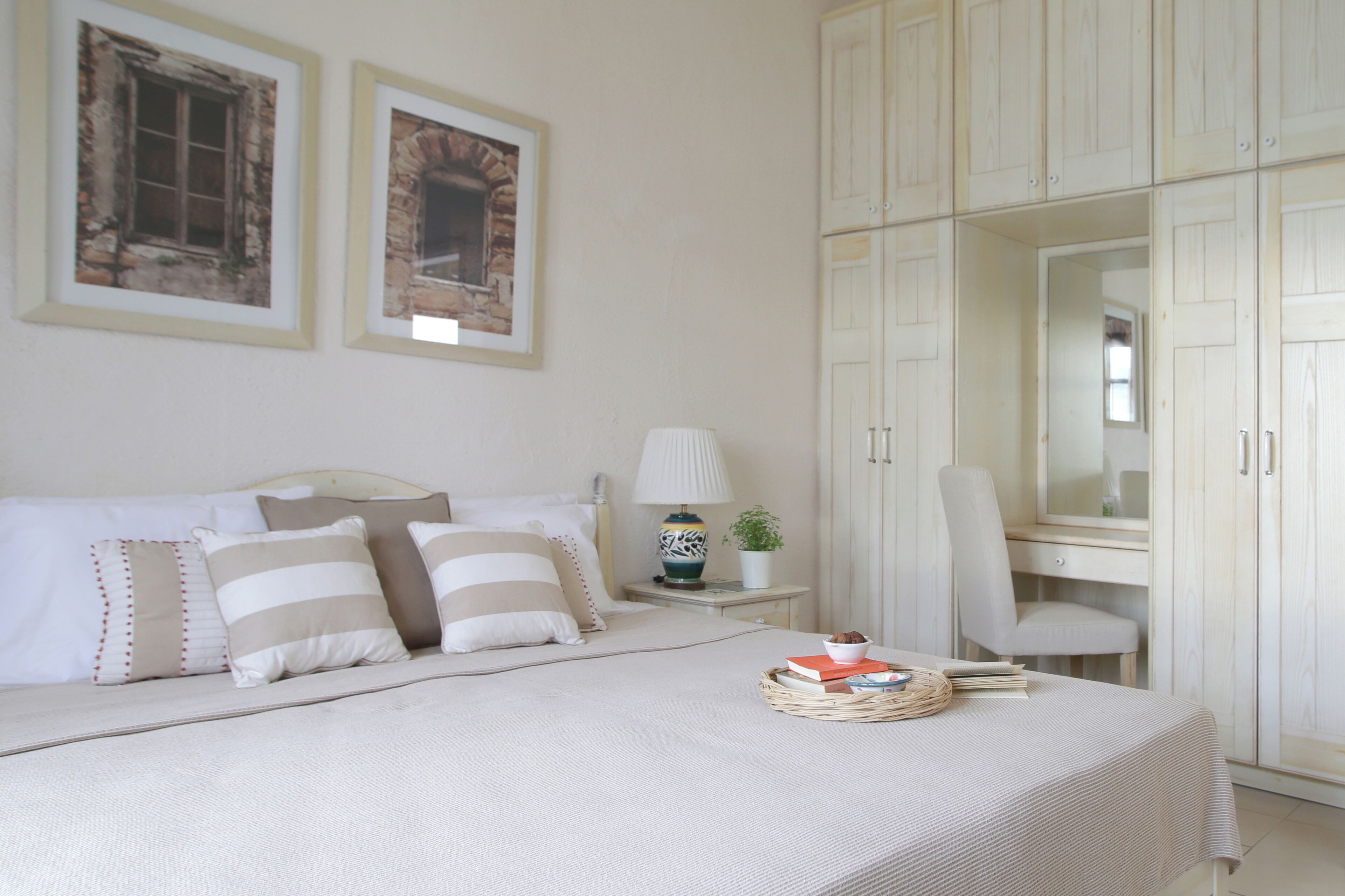 A bedroom with a bed, pillows, a bedside table with a lamp, a chair, and a wardrobe.
