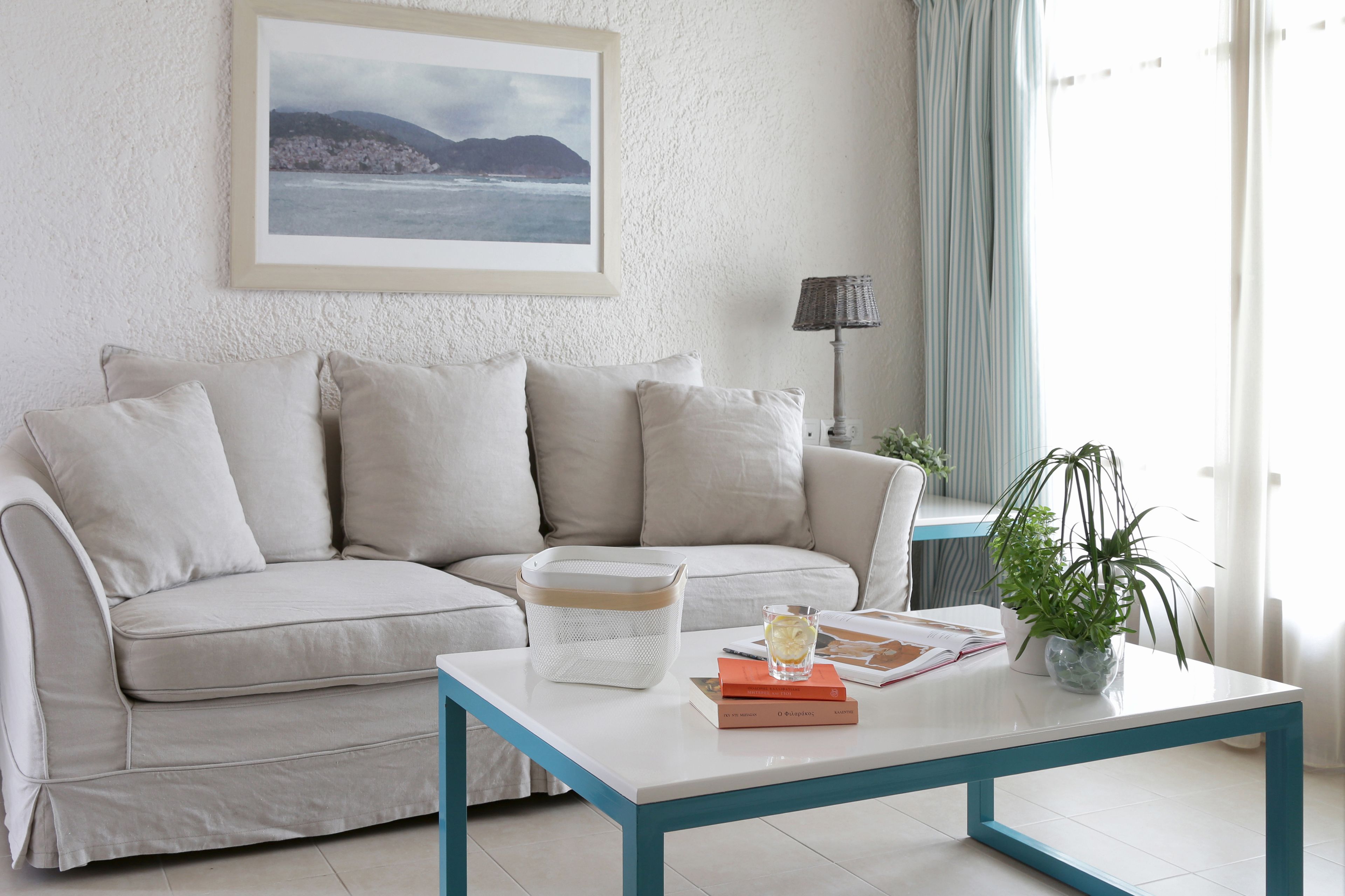 Ein Wohnzimmer mit einer Couch, einem Couchtisch, einem gerahmten Bild an der Wand, einer Lampe und einer Pflanze.