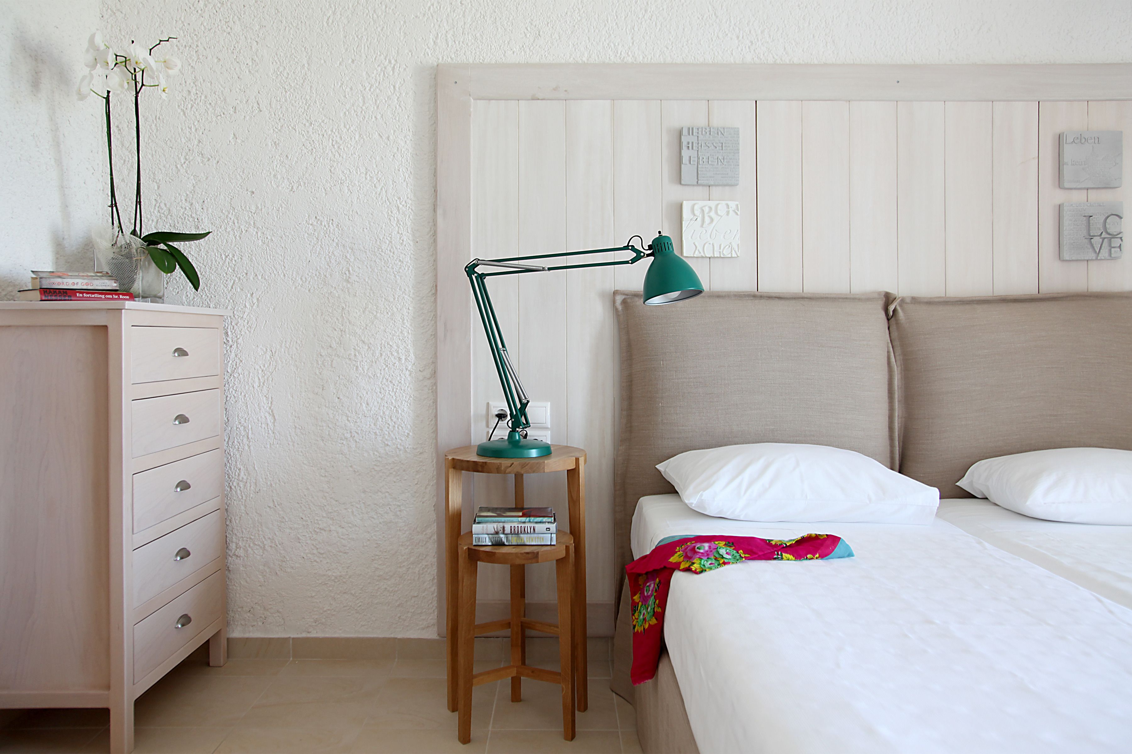 A bedroom with a bed, a nightstand, a desk, and a lamp.