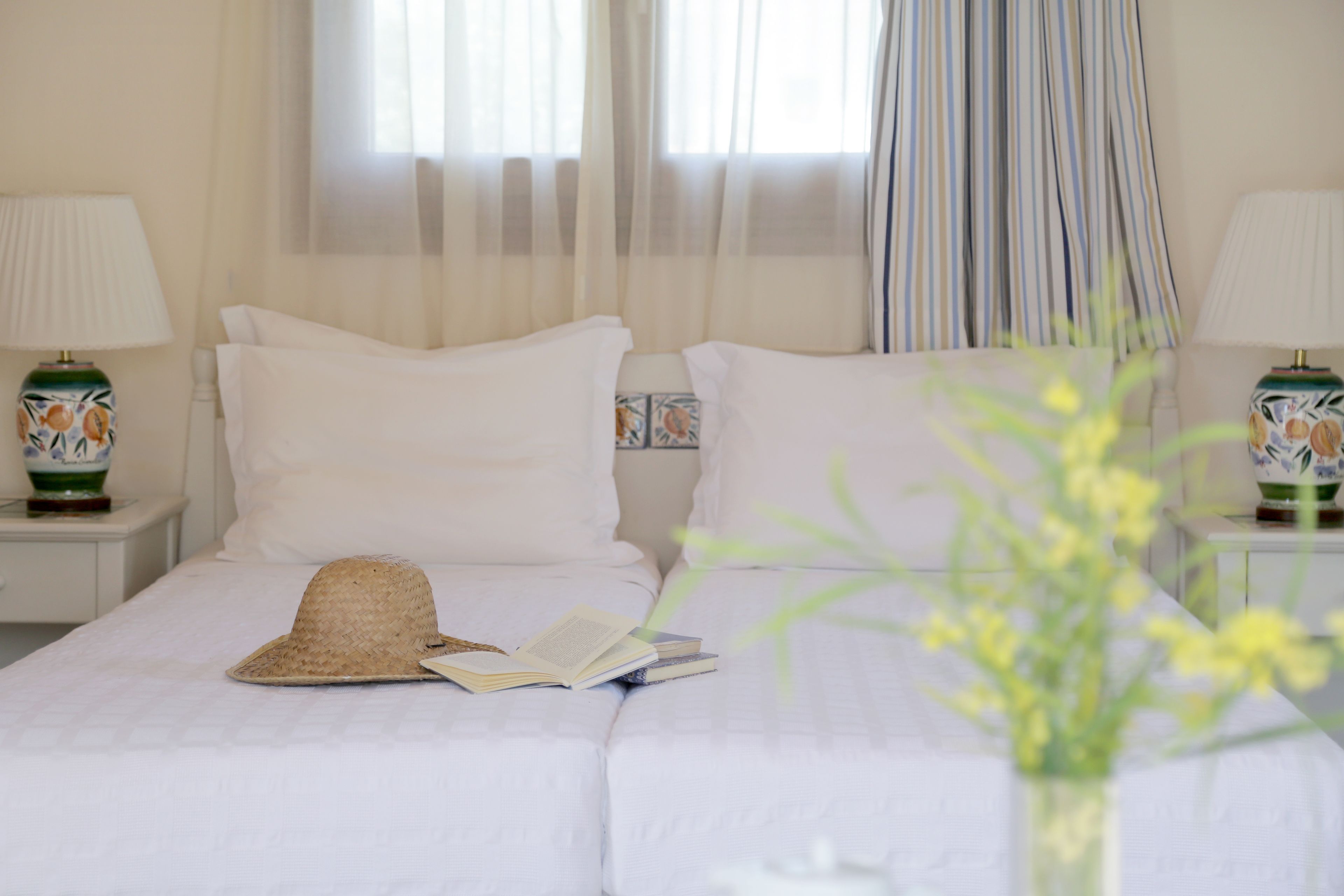 A neatly made bed with white linens, a straw hat, and a book on the pillows.